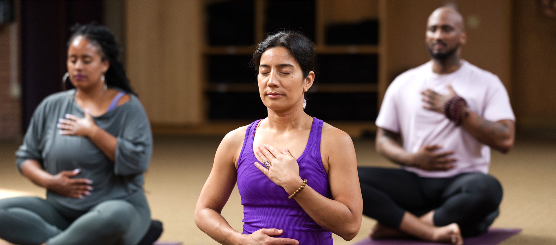 A class sits in meditation with their hands over their heart and stomach