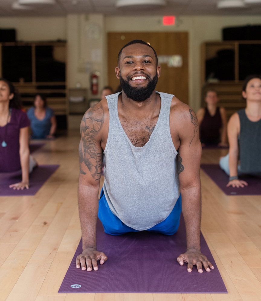 A man of color does yoga on a purple mat in the Kripalu studio.